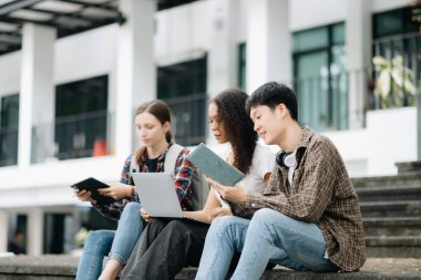 Öğrenciler merdivenlerde birlikte çalışıyorlar. Kitap okumak, dizüstü bilgisayar, tablet ve merdivenlerde otururken iletişim kurmak. 