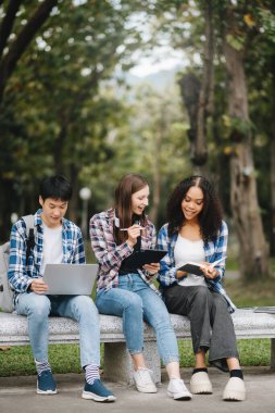 Öğrenciler kampüs parkını inceliyor. Gençler birlikte vakit geçiriyorlar. Tutma kitabı, dizüstü bilgisayar ve tablet 