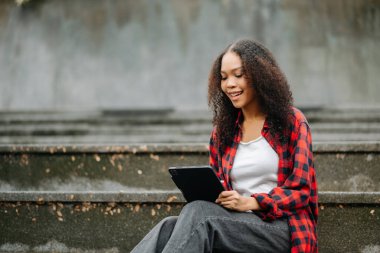 Afrika kökenli Amerikalı kız öğrenci merdivenlerde tablet kullanıyor. 