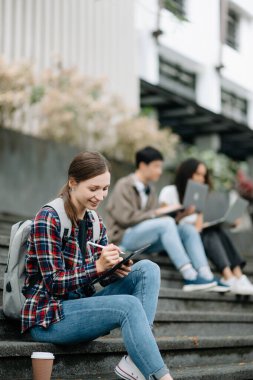 Genç üniversite öğrencileri sabahları kampüs parkında ders çalışıyor. Birlikte vakit geçirmek, dijital tablet kullanmak. 