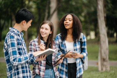 Gülümseyen öğrenciler birlikte kampüs parkını inceliyorlar. Tutma kitabı, tablet ve akıllı telefon 