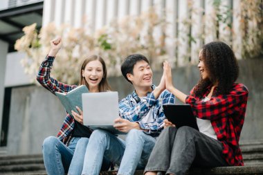 Kampüs parkında birlikte okuyan genç üniversite öğrencileri. Mutlu arkadaşlar projelerinin başarısını kutluyor.
