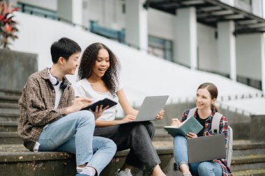 Öğrenciler merdivenlerde birlikte çalışıyorlar. Kitap okumak, dizüstü bilgisayar, tablet ve merdivenlerde otururken iletişim kurmak. 