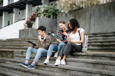 Öğrenciler merdivenlerde birlikte çalışıyorlar. Kızlar kitap okuyor, oğlanlar tablet çalışıyor. 
