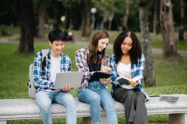 Öğrenciler kampüs parkını inceliyor. Gençler birlikte vakit geçiriyorlar. Tutma kitabı, dizüstü bilgisayar ve tablet 