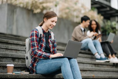 Öğrenciler merdivenlerde birlikte dizüstü bilgisayar kullanarak çalışıyorlar. 