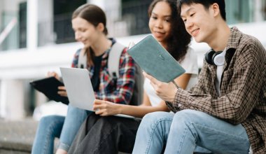Kampüs parkını araştıran çeşitli öğrenciler. Gençler birlikte kitap okuyarak ve tablet bilgisayar kullanarak zaman geçiriyorlar. Eğitim ve iletişim kavramı