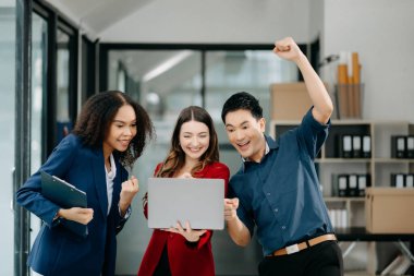 Bir grup genç iş adamı, takım çalışması laptopla başarıyı kutluyor ve ofiste yaratıcı tasarım planlıyor.