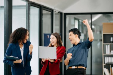 Bir grup genç iş adamı, takım çalışması laptopla başarıyı kutluyor ve ofiste yaratıcı tasarım planlıyor.
