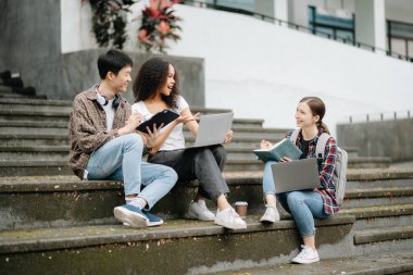 Öğrenciler merdivenlerde birlikte çalışıyorlar. Kitap okumak, dizüstü bilgisayarlarla çalışmak, tablet ve merdivenlerde otururken iletişim kurmak. 