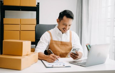 Genç erkek işyeri sahibi paket kutuları hazırlıyor ve çevrimiçi müşterilere, Alışveriş İnternetine ve küçük işletme konseptine teslimat yapmak için online siparişleri kontrol ediyor. 