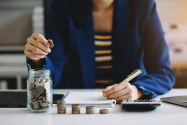 İş kadını elinde bozuk para tutarken hesap makinesi kullanarak ofiste finans muhasebesi için tasarruf parası hesaplıyor.