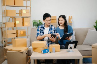 Başlangıçta küçük işletme KOBİ 'si, girişimci erkek ve kadın tablet kullanan girişimci, evdeki kanepede paket ürün kutusu hazırlamak için çevrimiçi alışveriş siparişini alır ve kontrol eder