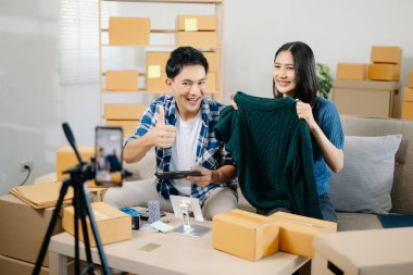 Giysilerini kameranın önünde gösteren iki Asyalı blogcu onun dükkanında canlı video kaydı yapıyor. Online Alışveriş Arabası kavramı. Evdeki kanepede.