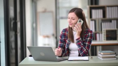 Bilgisayarla çalışan ve ofisteki akıllı telefondan konuşan Kafkasyalı iş kadını. 