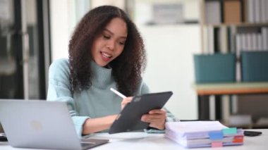Ofiste dizüstü bilgisayarla çalışan ve tablet bilgisayarına not alan mutlu Afrikalı iş kadını. 
