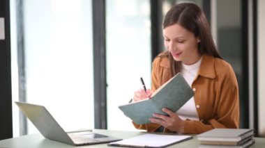 Ofiste dizüstü bilgisayarla çalışan ve not defterine not alan Kafkasyalı mutlu iş kadını. 