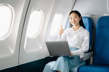 Çekici Asyalı kadın uçak yolcusu dizüstü bilgisayarda kablosuz bağlantıyla çalışırken rahat koltukta oturuyor. Stil içinde seyahat et, zarafetle çalış.