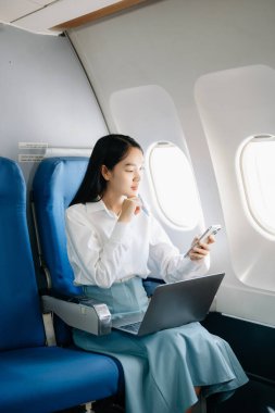 Çekici Asyalı kadın uçak yolcusu dizüstü bilgisayarda kablosuz bağlantıyla çalışırken rahat koltukta oturuyor. Stil içinde seyahat et, zarafetle çalış.