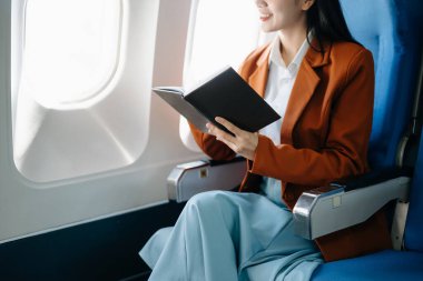 Çekici Asyalı kadın uçak yolcusu kitap okurken rahat koltukta oturuyor. Stil içinde seyahat et, zarafetle çalış.