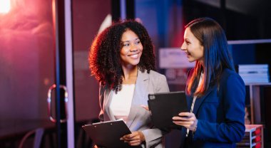 Yönetici yönetici, iş çözümlerini modern ofiste Afrikalı kadın pazarlama yöneticisiyle tablet üzerinde fikirler paylaşır ve tartışır. Karanlık zamanlarda neon ışığı