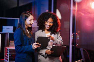 Yönetici yönetici, iş çözümlerini modern ofiste Afrikalı kadın pazarlama yöneticisiyle tablet üzerinde fikirler paylaşır ve tartışır. Karanlık zamanlarda neon ışığı