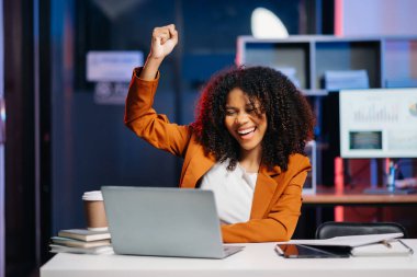  İş kadını ofisteki dizüstü bilgisayarında çalışmaktan memnun ve mutlu. Karanlık zamanlarda neon ışığı