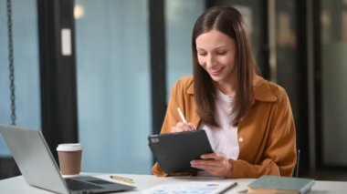 Ofiste dizüstü bilgisayarla çalışan ve not alan Kafkasyalı mutlu iş kadını