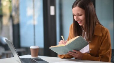 Ofiste dizüstü bilgisayarla çalışan ve not alan Kafkasyalı mutlu iş kadını