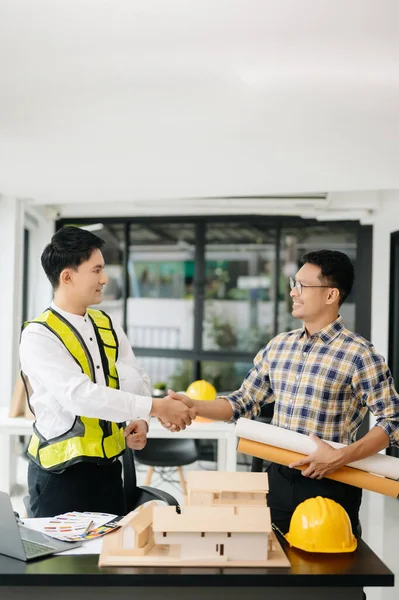 Construction team shake hands greeting start new project plan behind yellow helmet on desk in office center to consults about their building project