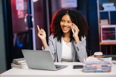 İş kadını fazla mesai yapıyor bilgisayar ve akıllı telefon kullanıyor, lamba ışığında fazla mesai yapıyor.