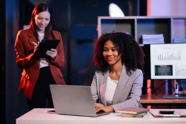 Yönetici yönetici, iş çözümlerini modern ofiste Afrikalı kadın pazarlama yöneticisiyle tablet üzerinde fikirler paylaşır ve tartışır. Karanlık zamanlarda neon ışığı