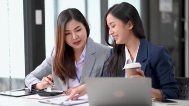 Modern ofiste doküman ve hesap makinesiyle birlikte çalışan iki Asyalı iş kadını
