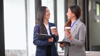 Modern ofiste kahve içerken sohbet eden iki Asyalı iş kadını.
