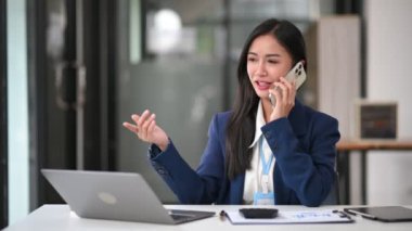  Güzel Asyalı iş kadını cep telefonuyla konuşuyor. İş yerinde oturuyor, video çekiyor.