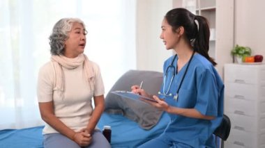 Asyalı doktor hastanedeki Asyalı yaşlı kadını muayene ederken not alıyor.