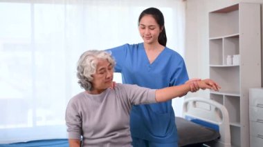 Asyalı fizyoterapist, yaşlı bir kadının hastayla el ele çalışmasına yardım ediyor.