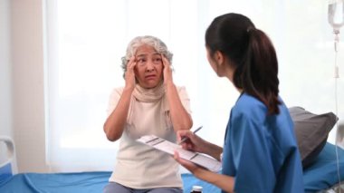 Asyalı doktor hastanedeki Asyalı yaşlı kadını muayene ederken not alıyor.