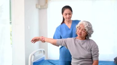 Asyalı fizyoterapist, yaşlı bir kadının hastayla el ele çalışmasına yardım ediyor.