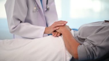 Beyaz takım elbiseli Asyalı doktor hastanede yatağında yatan Asyalı yaşlı kadını muayene ediyor.