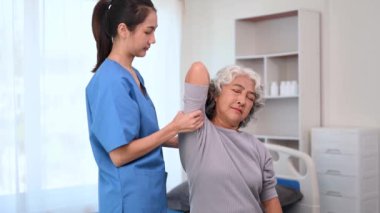 Asyalı fizyoterapist, yaşlı bir kadının hastayla el ele çalışmasına yardım ediyor.