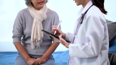 Asyalı doktor hastanedeki Asyalı yaşlı kadını muayene ederken not alıyor.
