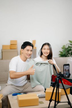 Giysilerini kameranın önünde gösteren iki Asyalı blogcu onun dükkanında canlı video kaydı yapıyor. Online Alışveriş Arabası kavramı. Evdeki kanepede.