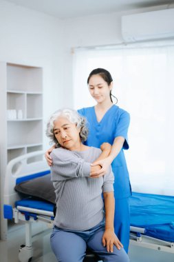 Asyalı fizyoterapist hastane ofisinde egzersiz yaparken kadın hastanın kolunu esnetmesine yardım ediyor.