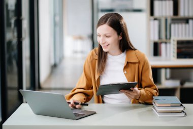Genç ve güzel bir kadın laptopta çalışırken beyaz masadaki modern ofiste çalışıyor.