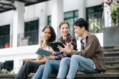 Genç üniversite öğrencileri parktaki merdivenlerde tablete bakarak ders çalışıyor. 