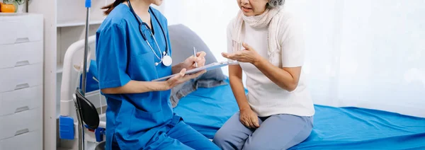 Asian doctor taking notes while examining Asian elderly woman patient in hospital