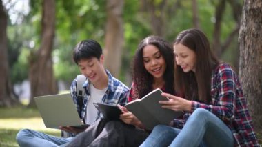 Kampüs parkında birlikte okuyan genç üniversite öğrencileri çimlerin üzerinde oturuyorlar.