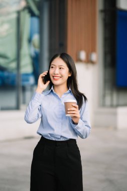 Genç Asyalı iş kadını arka planda iş merkezi olan büyük şehirde akıllı telefon kullanıyor. 