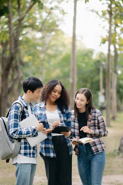 Diverse students studying the campus park. Young people are spending time together reading book and using tablet pc. Education and communication concept